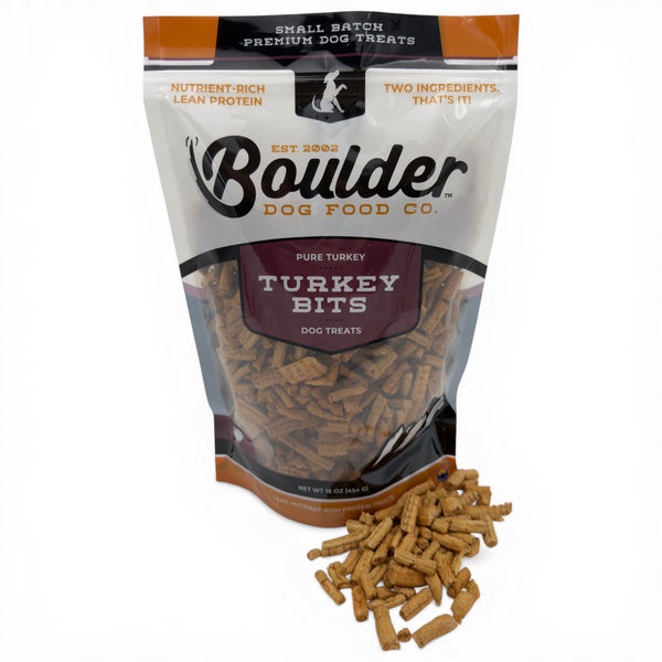 Bag of Boulder Dog Food Co. Turkey Bits dog treats with some treats spilling out on a white background.