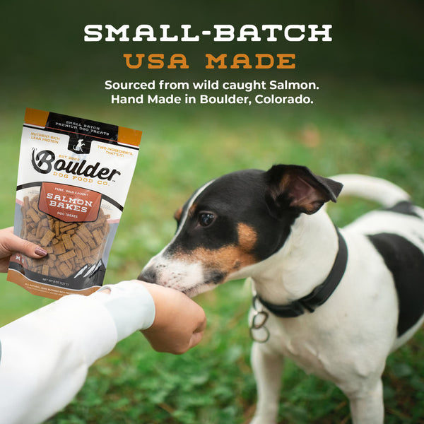 Dog being offered a treat from a Boulder Pet Food bag with text about small-batch USA-made products.